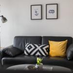 Schwarzes Sofa mit Kissen, Stehlampe und Wandbildern.