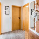 Flur mit Holztüren, Spiegel und Kleiderhaken. Wandbilder und Holzschrank sind sichtbar.