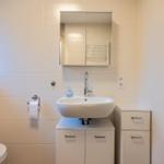 Badezimmer mit Waschbecken, Spiegel, Toilette und Handtuchhalter.