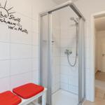 Duschbereich mit Duschkabine und roten Sitzkissen an der Wand.