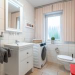 Badezimmer mit Waschmaschine, Toilette und Fenster mit Streifenrollo.