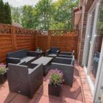 Terrasse mit Sitzgruppe, Pflanzen und Holzgeländer. Durchgang zur Wohnung mit Sofa.