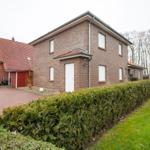Zweistöckiges Haus mit Garten und Terrasse. Roter Dachfirst und Ziegelmauer.