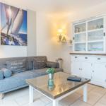 Ein Wohnzimmer mit grauem Sofa, Glas-Tisch und weißem Schrank. Wandbild zeigt Segelboot.