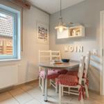 Essbereich mit runden Tisch, weißen Stühlen und rot-weißen Sitzkissen. Durchgang zum Wohnzimmer.