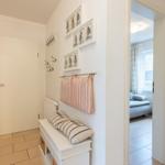 Eingangsbereich mit Kleiderhaken, Bildern und Sitzbank. Durchgang zu Wohnzimmer mit Sofa.