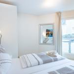 Schlafzimmer mit Bett, Fenster und Wandbild. Decke und Kissen sind gestreift.