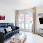 Wohnzimmer mit Sofa, Glas-Tisch und Fernseher. Durchgangstür zum Balkon.
