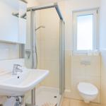 Badezimmer mit Dusche, Waschbecken und WC. Fenster sorgt für Tageslicht.