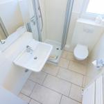 Badezimmer mit Dusche, Waschbecken und Toilette. Fenster und Heizung sind sichtbar.