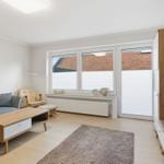 Wohnzimmer mit Sofa, Couchtisch und TV. Fenster mit Jalousien und Wandbild.