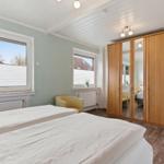 Schlafzimmer mit Doppelbett, Holzschrank und Fenstern mit Jalousien.