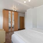 Schlafzimmer mit Bett, Kleiderschrank und Sessel. Wandbilder und Holzboden.
