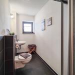 Badezimmer mit Toilette, Waschbecken und Dusche. Fenster, Bilder und Handtücher sind sichtbar.