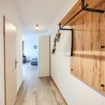 Flur mit Holzwand und Tür. Im Hintergrund ist ein Schlafzimmer mit Bett und Sofa.