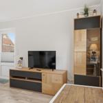 Wohnzimmer mit Fernseher, Schrank und Fenster. Holzmöbel und helle Wände.