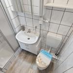 Badezimmer mit Dusche, Waschbecken und Toilette mit Strandmotivdeckel.