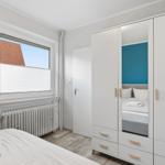 Schlafzimmer mit weißem Schrank, Bett und Fenster mit Blick auf Dach.