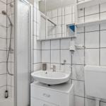 Badezimmer mit Dusche, Waschbecken und Toilette. Weiße Fliesen und Spiegelschrank.