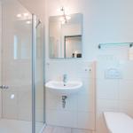 Badezimmer mit Dusche, Waschbecken und Toilette. Weiße Fliesen und Spiegel.