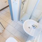 Badezimmer mit Dusche, Waschbecken und Toilette. Fliesenboden und weiße Einrichtung.