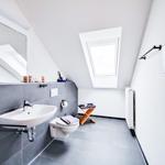 Dusche mit Dachfenster, Spiegel und Toilette in einem schrägen Dachbodenbad.