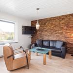 Wohnzimmer mit Sofa, Sessel, Couchtisch und Holzwand. Fenster mit Blick nach draußen.