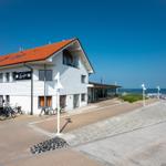 Ein weißes Gebäude mit rotem Dach steht am Strand. Fahrräder sind vor dem Haus abgestellt.