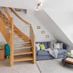 Wohnzimmer mit Sofa, Glas-Tisch und Holztreppe unter Dachschräge