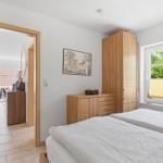Schlafzimmer mit Doppelbett, Holzschrank und Fenster mit Blick auf Grün.