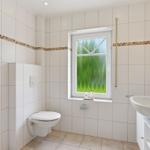 Badezimmer mit Dusche, Toilette und Waschbecken. Fenster mit grünem Glas.