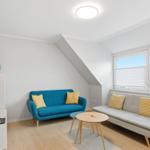 Wohnzimmer mit blauem Sofa, grauem Sofa und Holztisch. Fenster mit Jalousien und TV.