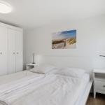 Schlafzimmer mit weißem Bett, Kleiderschrank und Wandbild. Zwei Nachttische mit Lampen.