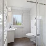 Badezimmer mit Dusche, Toilette und Waschbecken. Fenster mit getöntem Glas.