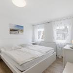 Schlafzimmer mit weißem Bett, Nachttischen und Fenster mit weißen Vorhängen.