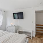 Schlafzimmer mit Bett, Schrank, Fernseher und Fenster mit Vorhängen.