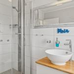 Badezimmer mit Dusche, Waschbecken und Spiegel. Wanddekoration mit Moin.