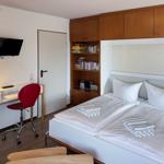 Zimmer mit Doppelbett, Schreibtisch, roter Stuhl und Wandfernseher.