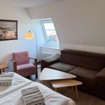 Zimmer mit Sofa, Sessel, Tisch und Bett. Fenster mit Blick auf Dach.