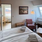 Zimmer mit Bett, Sessel und Fenster. Blick auf Dach und Wasser.