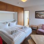 Schlafzimmer mit Doppelbett, Holzmöbeln und rosa Sessel.