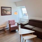 Wohnzimmer mit braunem Sofa, rosa Sessel, Tisch und Fenster