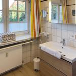 Badezimmer mit Waschbecken, Spiegel und Fenster mit Blick auf Garten.