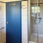 Badezimmer mit Dusche, blauer Tür und Wanduhr.
