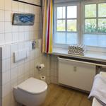 Badezimmer mit Toilette, Waschbecken und Fenster mit bunten Vorhängen.