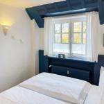 Ein Schlafzimmer mit weißem Bett, blauem Fensterbrett und Fenster mit weißen Vorhängen.