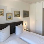 Schlafzimmer mit Doppelbett, weißen Bettwäsche, Wandbildern und Schrank.