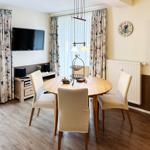 Rundes Esszimmer mit Holztisch, vier Stühlen und TV-Wand. Holzfußboden und Vorhänge.