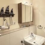 Badezimmer mit Waschbecken, Spiegelschrank und Wandhalterung für Handtuch und Haartrockner.