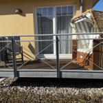 Terrasse mit Hängesessel und Gittergeländer vor gelbem Haus mit Fenster.